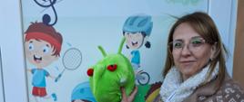 Inspektor stojąca na tle kolorowych do przedszkola i trzymająca w ręce maskotkę PESTY 