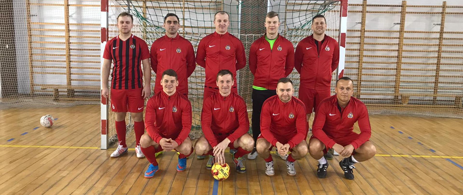 Zwycięstwo sokołowskich strażaków w eliminacjach do XIX Mistrzostwach Województwa Mazowieckiego Strażaków PSP w Halowej Piłce Nożnej - zawodnicy w strojach sportowych na sali gimnastycznej stoją na zbiórce przed bramką