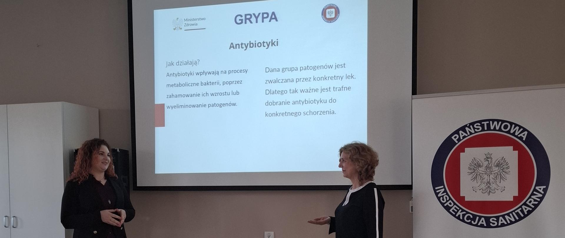 Pracownicy Powiatowej Stacji Sanitarno-Epidemiologicznej w Garwolinie w trakcie prezentacji, na tle slajdu o grypie i logo Państwowej Inspekcji Sanitarnej.