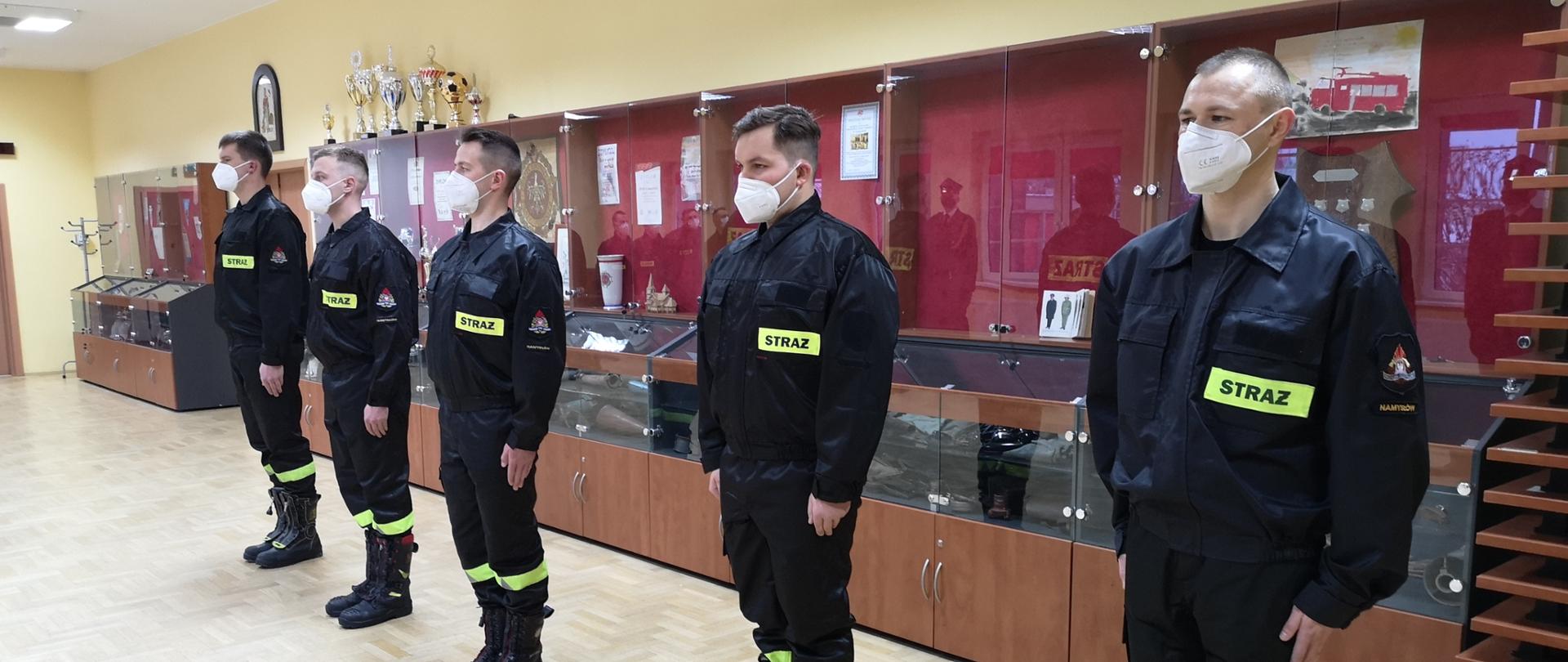 Strażacy w szyku podczas ślubowania w umundurowaniu koszarowym, w obuwiu specjalnym zabezpieczeni w maseczki FPP2.