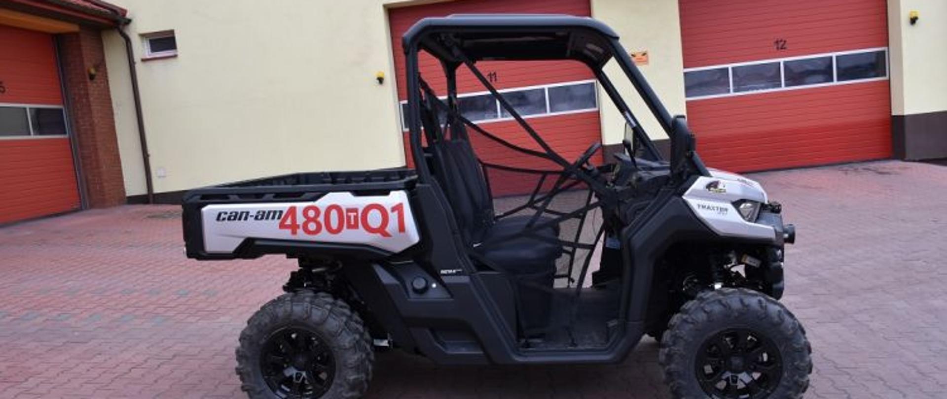 Widok z boku zakupionego Quada przez KP PSP w Skarżysku-Kamiennej. Na zdjęciu widać bok burty bagażowej na której na białym tle znajduje się numer operacyjny w formie czerwonego napisu. Widać również bok szoferki pojazdu wewnątrz której znajdują się dwa fotele w kolorze czarnym dla kierowcy i pasażera. Pojazd stoi na tle czerwonych bram garażowych komendy powiatowej PSP w Skarżysku-Kamiennej.