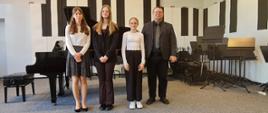 Mężczyzna i trzy nastolatki stoją na scenie przed fortepianem.