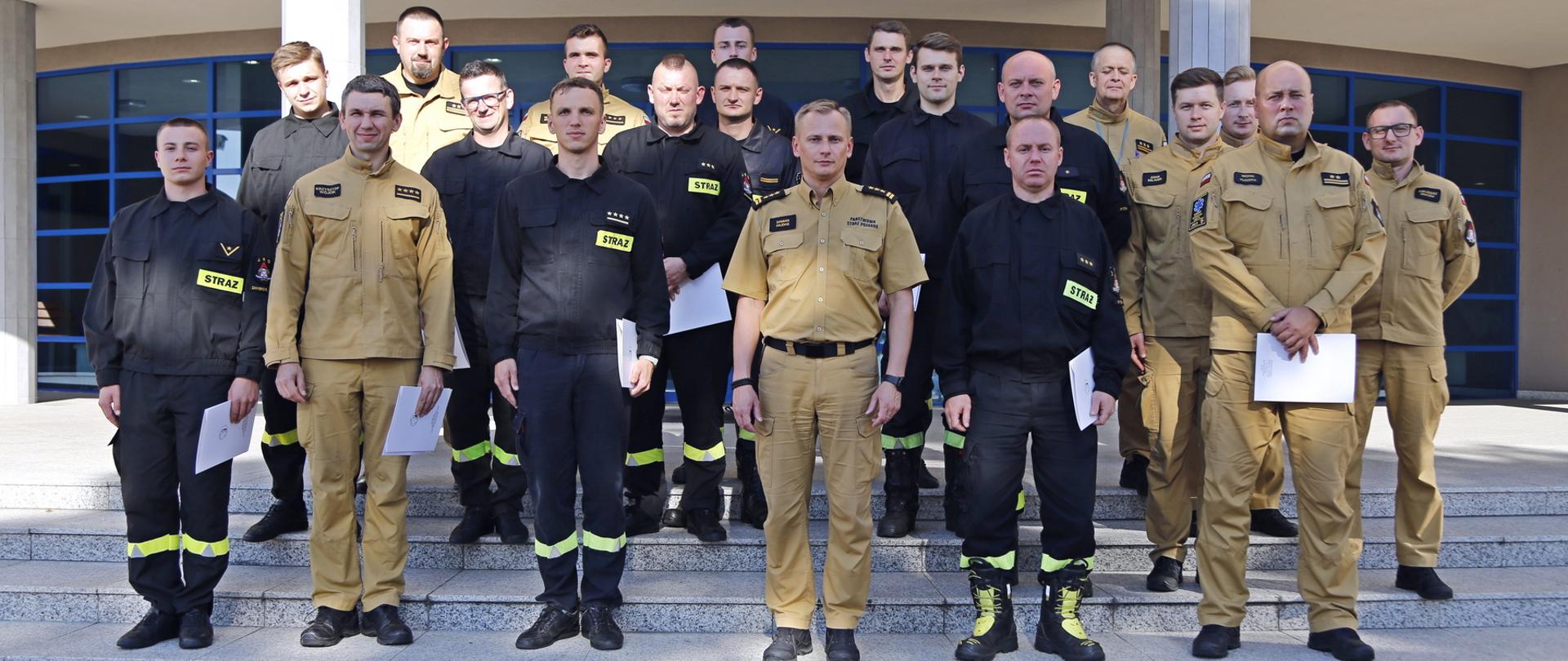 Grupowe zdjęcie uczestników szkolenia (16 funkcjonariuszy PSP) w towarzystwie Zastępcy Komendanta Centralnej Szkoły PSP oraz dwóch funkcjonariuszy CS PSP