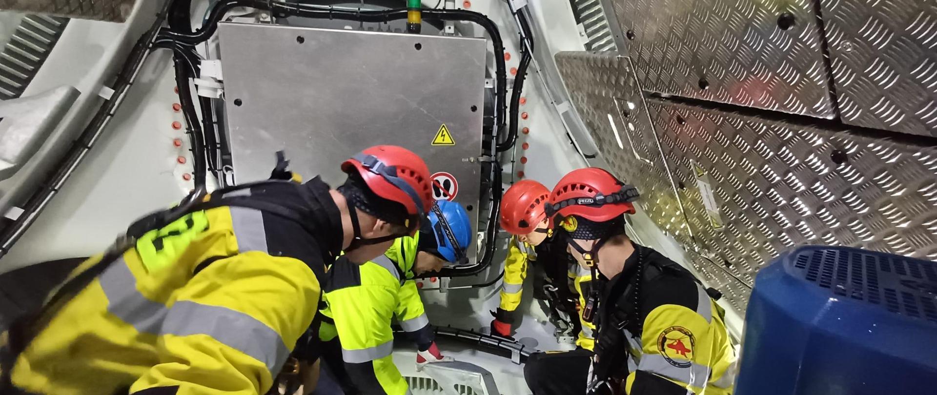 Czterech strażaków w kaskach na głowie spoglądają w dół