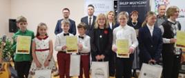 Grupa uczniów wraz jurorami konkursowymi pozują do zdjęcia grupowego trzymając nagrody oraz dyplomy za udział w Ogólnopolskim Konkursie Gitarowym o tytuł "Mistrza Sześciu Strun" w Oleśnicy - 13 stycznia 2024