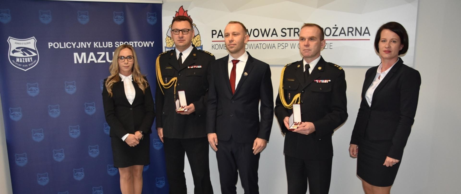 Odznaczeni i przedstawiciele Policyjnego Klubu Sportowego Mazury stoją do pamiątkowego zdjęcia.