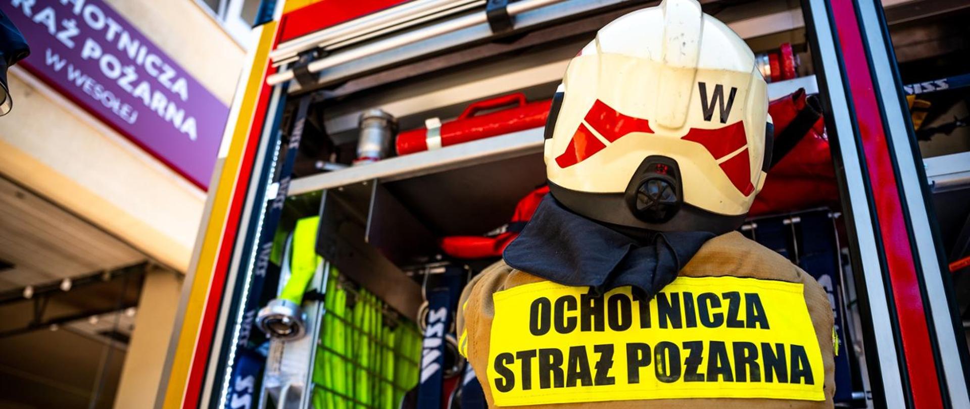 Strażak Ochotniczej Straży Pożarnej przy samochodzie ratowniczo-gaśniczym przygotowuje sprzęt do działań ratowniczych.