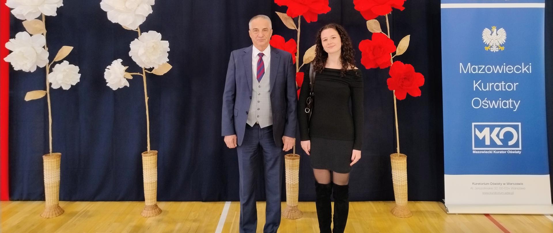 Stypendystka wraz z dyrektorem szkoły pozują na tle ścianki z napisem Stupendium Prezesa Rady Ministrów 2025-2026