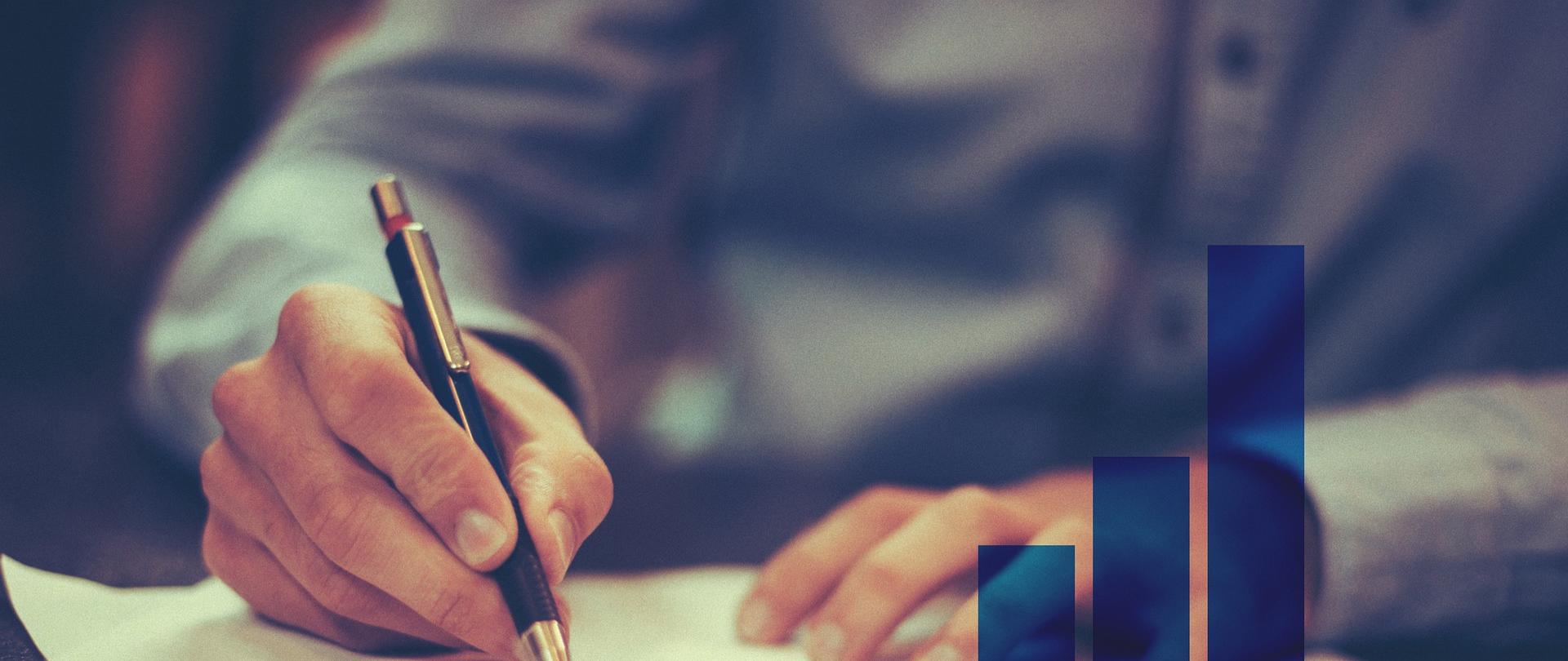 Zdjęcie w poziomie. Niebieski wykres. W tle mężczyzna piszący w notesie