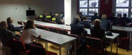 Szkolenie pocztów sztandarowych. Zdjęcie przedstawia świetlicę komendy w Rawiczu. Przy stołach siedzą uczestnicy szkolenia, którzy oglądają prezentację multimedialną, wyświetlaną na ekranach. Część uczestników ma na sobie mundury galowe, pozostali - koszarowe.