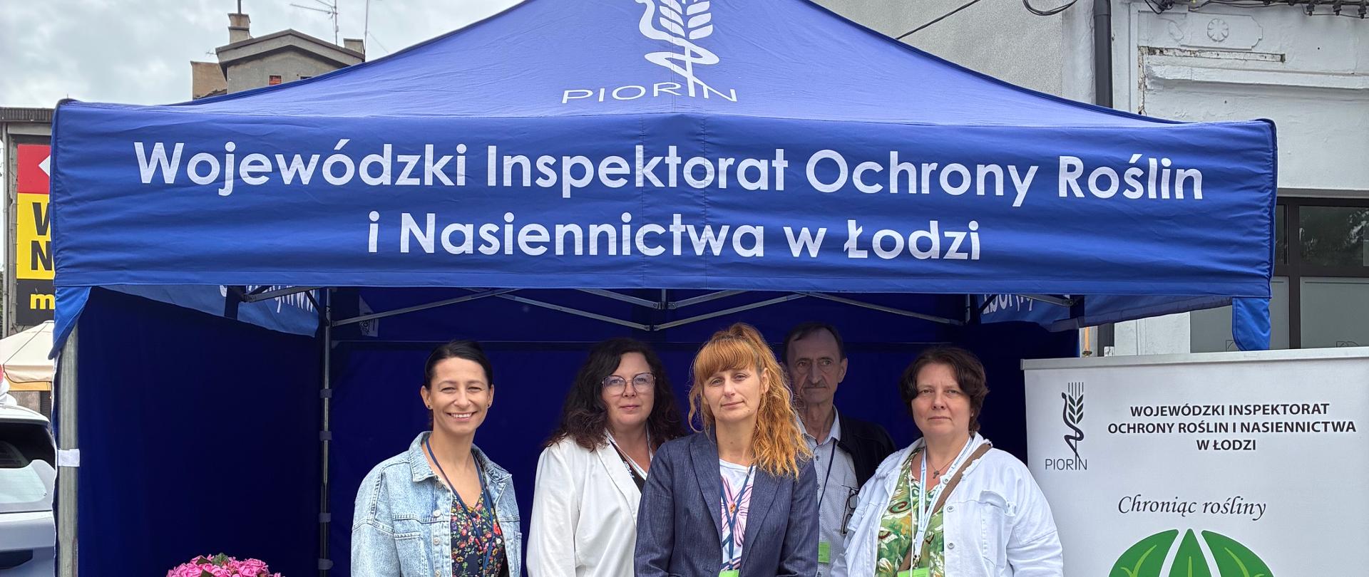Namiot z napisem „Wojewódzki Inspektorat Ochrony Roślin i Nasiennictwa w Łodzi”. Przed namiotem stoją cztery osoby ustawione do wspólnego zdjęcia i uśmiechają się do aparatu.