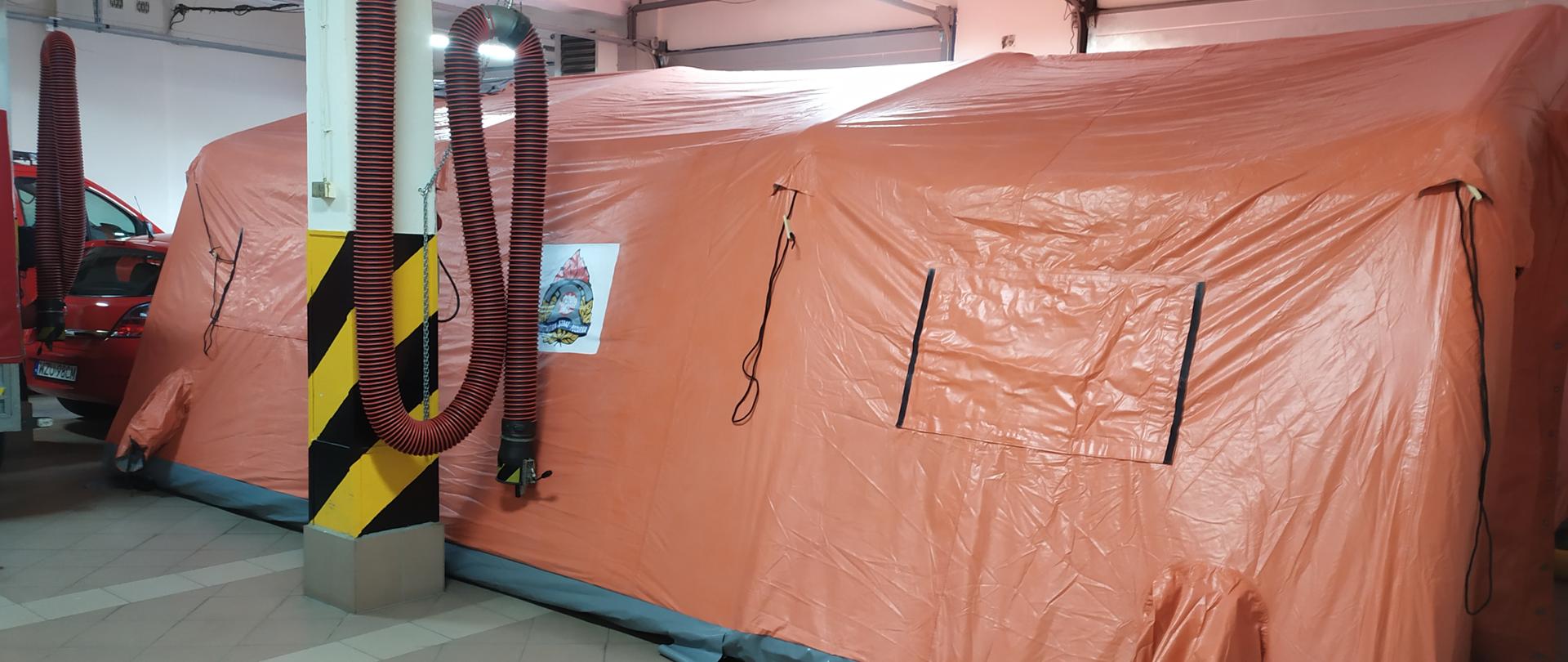 Namiot pneumatyczny pomarańczowy o siwym podłożu rozstawiony na garażu komendy.