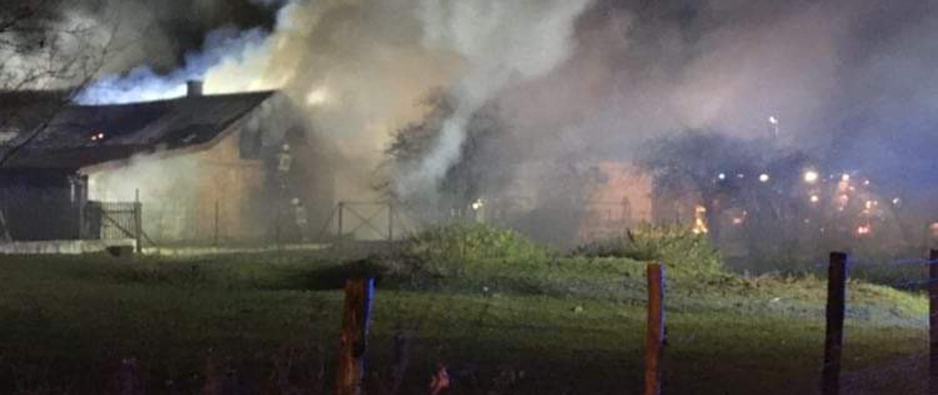 Zdjęcia powyżej przedstawiają palące się zabudowania gospodarcze, które w dużej części są objęte zadymieniem . Zdjęcie zrobione jest w nocy, przy lekko oświetlonym polu pracy. Przed budynkami widać łąkę, która jest ogrodzona kołkami drewnianymi. W prawej części zdjęcia widoczne z oddali oświetlenie ostrzegawcze innych zastępów uczestniczących w tym zdarzeniu. 