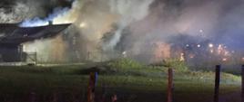 Zdjęcia powyżej przedstawiają palące się zabudowania gospodarcze, które w dużej części są objęte zadymieniem . Zdjęcie zrobione jest w nocy, przy lekko oświetlonym polu pracy. Przed budynkami widać łąkę, która jest ogrodzona kołkami drewnianymi. W prawej części zdjęcia widoczne z oddali oświetlenie ostrzegawcze innych zastępów uczestniczących w tym zdarzeniu. 