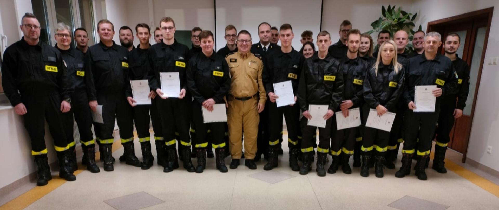 Zdjęcie przedstawia Zastępce Pomorskiego Komendanta Wojewódzkiego PSP, KomendantaPowiatowego PSP w Pruszczu Gdańskim oraz strażaków ochotników, którzy ukończyli szkolenie podstawowe strażaków ratowników Ochotniczych Straży Pożarnych