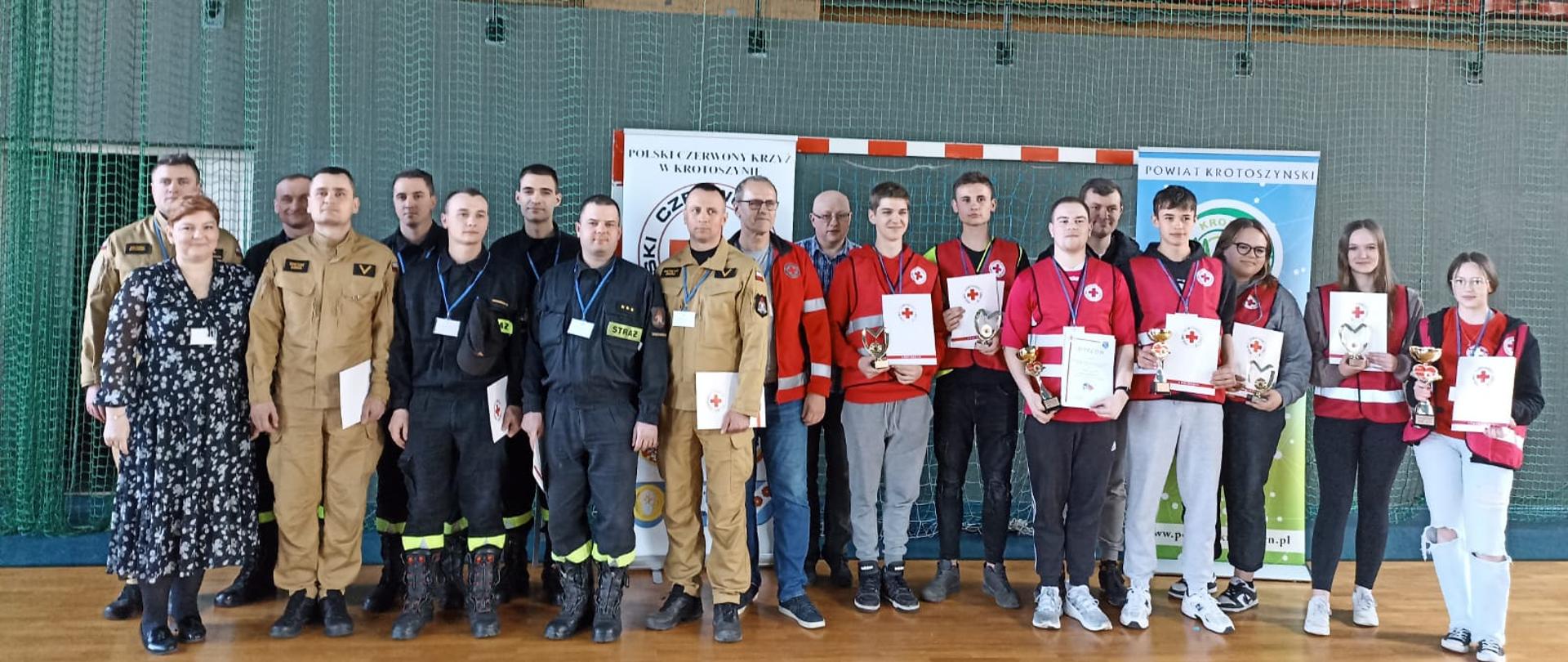 Zdjęcie grupowe przedstawia uczestników mistrzostw pierwszej pomocy oraz kadrę sędziowską i organizatorów przedsięwzięcia. Na fotografii widać strażaków w umundurowaniu przedstawicieli PCK w Krotoszynie, Starostwa Powiatowego oraz młodzież szkolną 