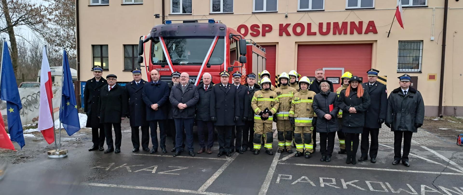 druhowie OSP Kolumna, strażacy PSP oraz zaproszeni goście pozują do zdjęcia na samochodu gaśniczego i budynku jednostki