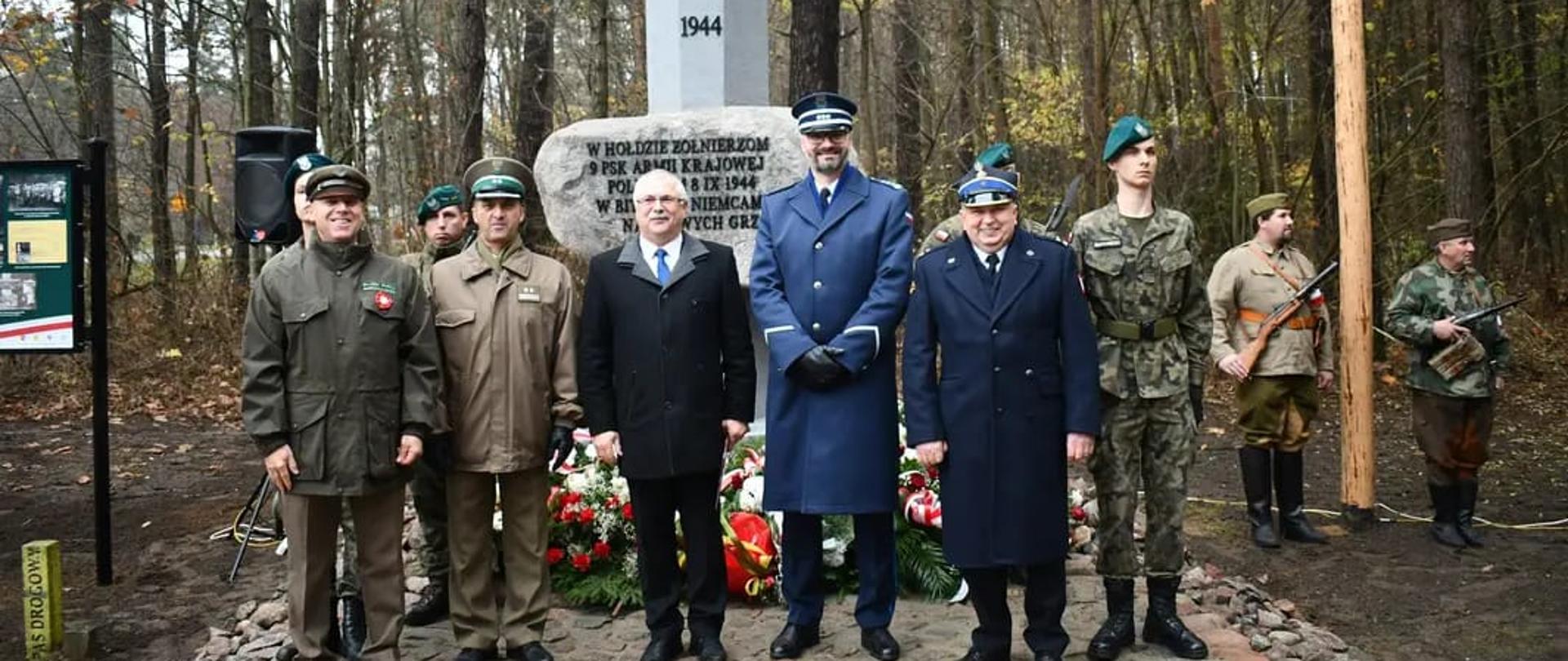 Obchody Święta Niepodległości w Tamie. Uczestnicy stoją i pozują do zdjęcia na tle pomnika. 