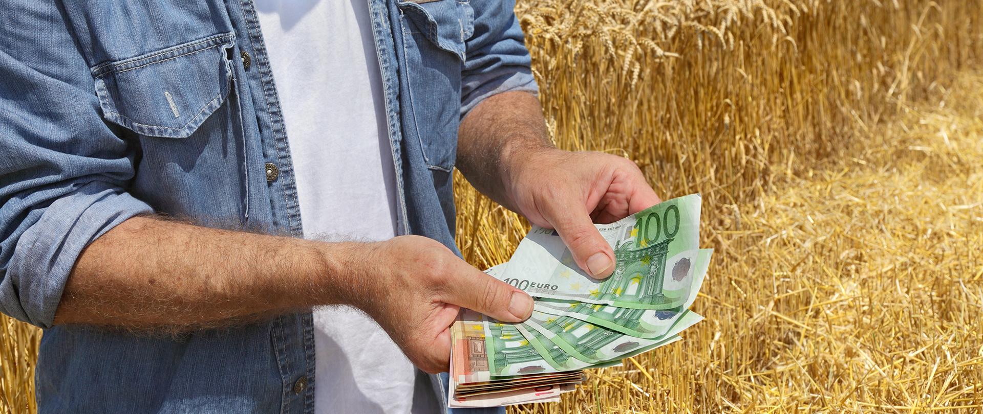 Farmer holding Euro banknote with combine harvester in background