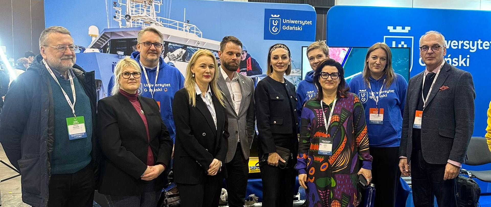 Targi edukacyjne. Przed tablicą z napisem Uniwersytet Gdański stoi kilka osób, w tym wojewoda pomorska 