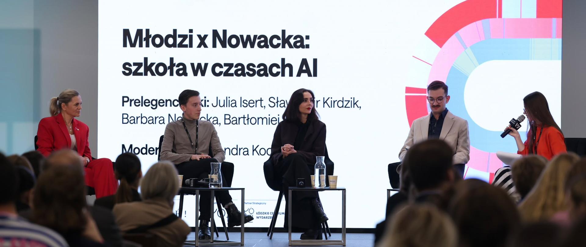 Minister Edukacji Barbara Nowacka siedzi i rozmawia z innymi uczestnikami wydarzenia.
