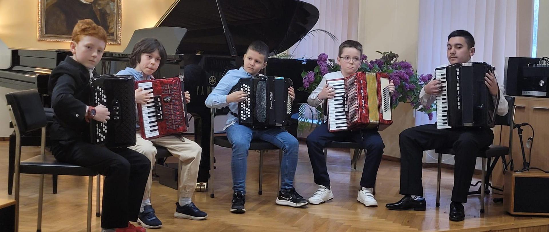 Galeria 15 zdjęć z koncertu uczniów klas akordeonu P. Liliany Stopki i P. Tomasza Brusińskiego, który odbył się 25 kwietnia 2024 w auli PSM w Kłodzku. Uczniowie grają na akordeonach na scenie auli.