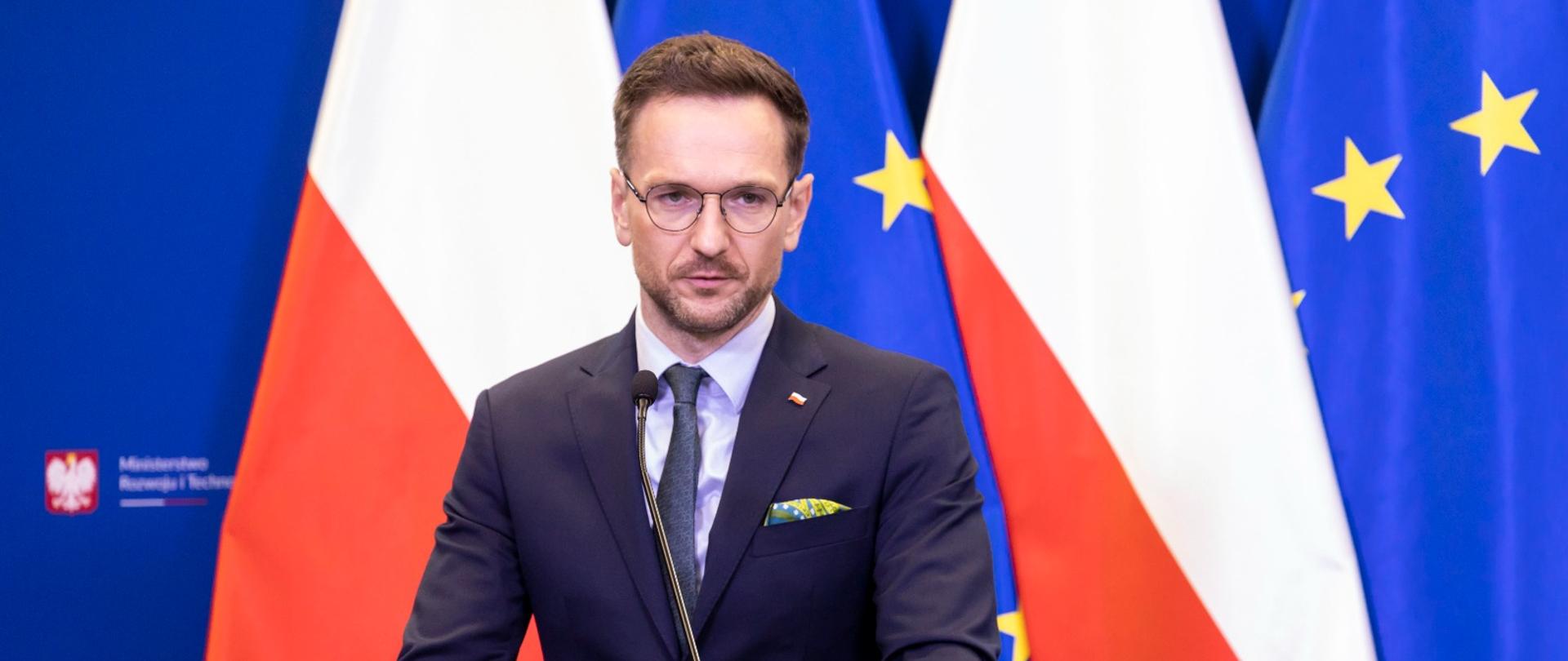 minister Waldemar Buda przy mównicy na tle flag PL i UE