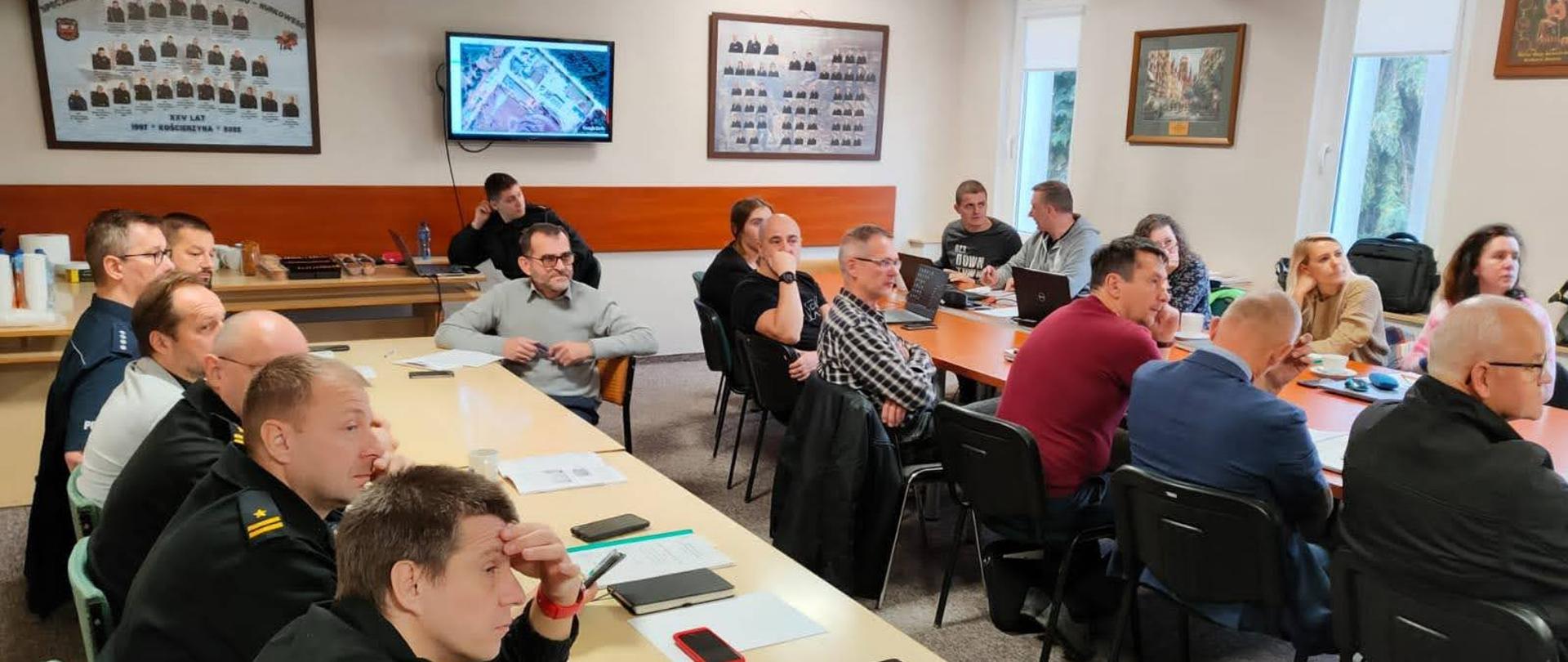 Uczestnicy ćwiczeń siedzą za stołami przed nimi są dokumenty oraz kartki papieru.