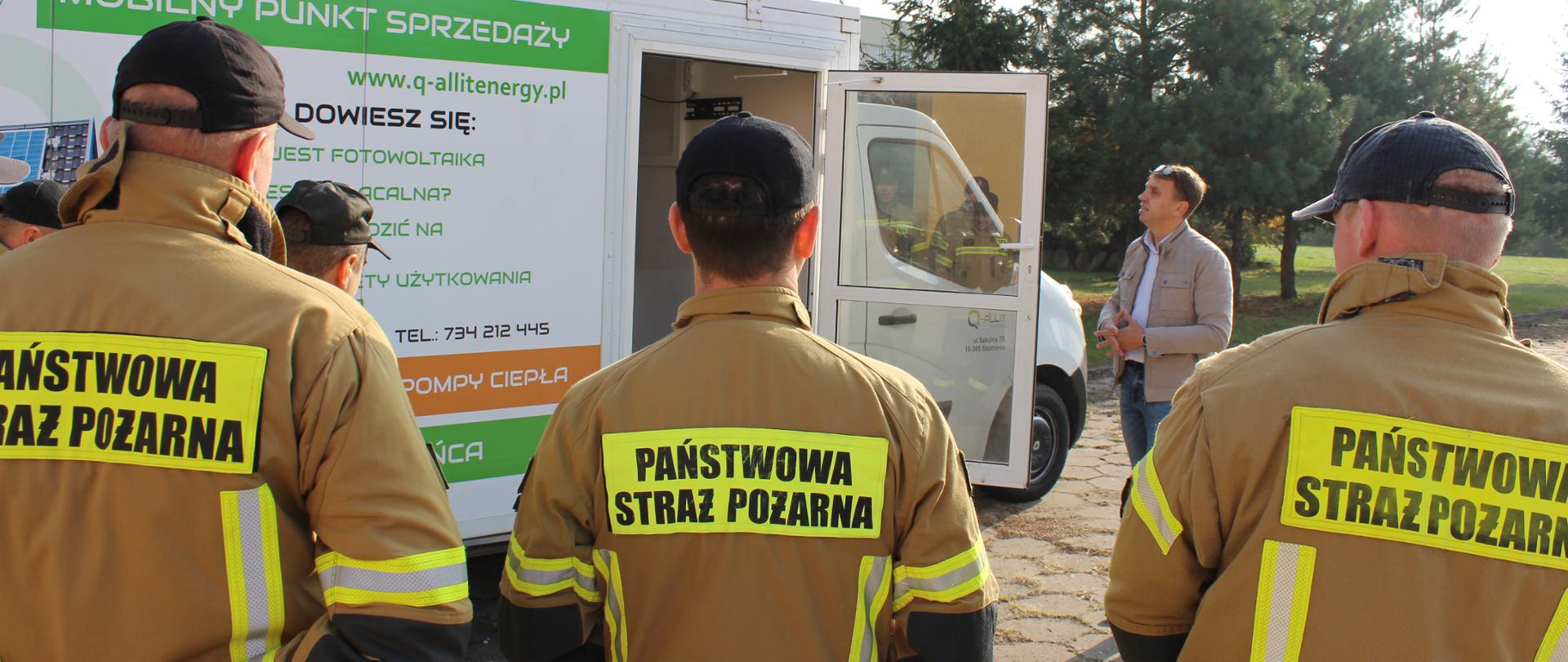 Strażacy słuchający wykładu na temat fotowoltaiki przed samochodem na zewnątrz