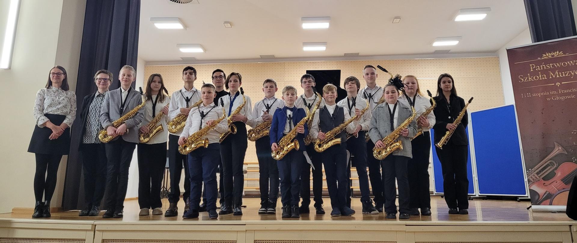 Uczestnicy koncertu z nauczycielami na scenie auli w Państwowej Szkole Muzycznej I i II stopnia im. Franciszka Liszta w Głogowie.