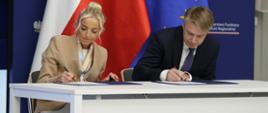Na zdjęciu dwie osoby prze stole konferencyjnym podpisuje dokumenty