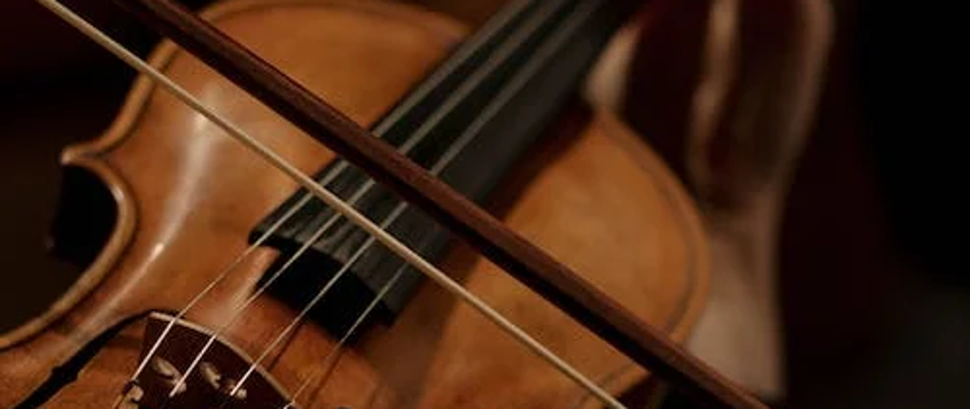 brązowe skrzypce, a na środku strun grający na nich smyczek