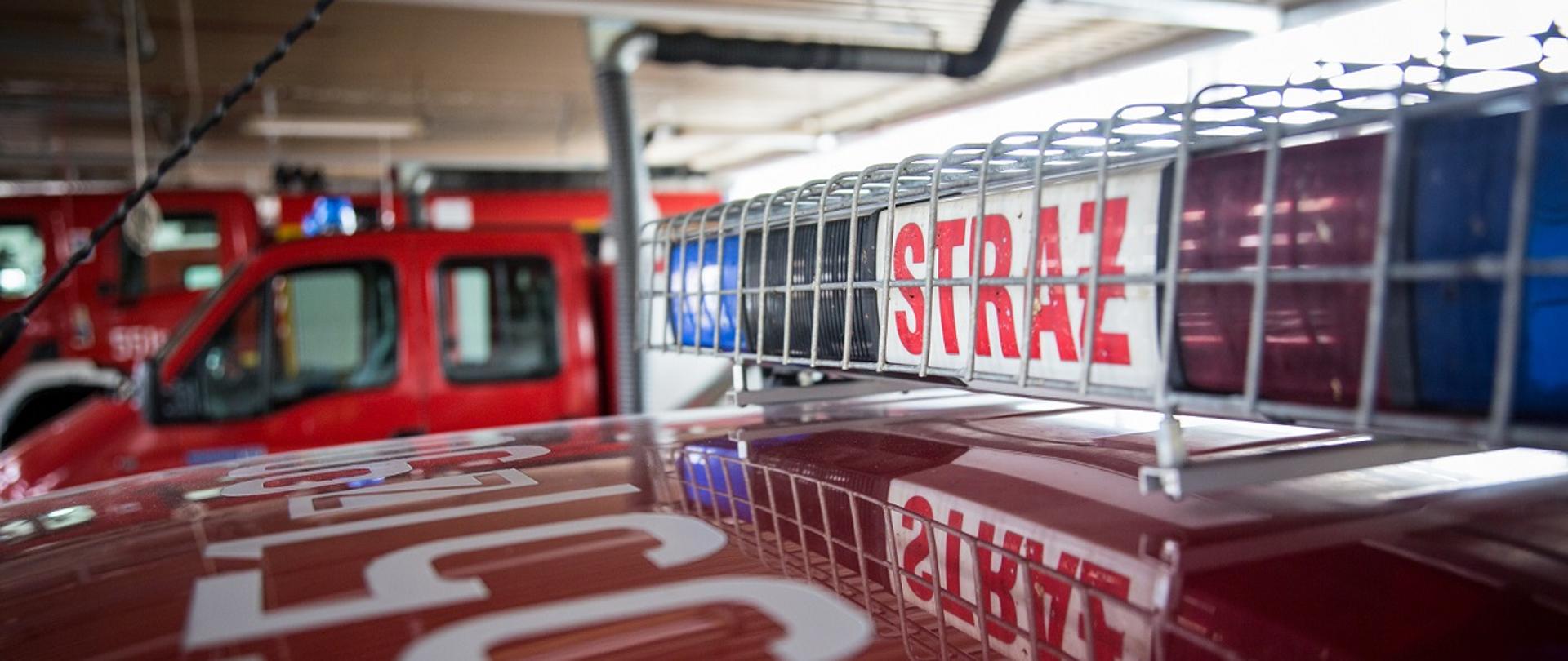 Zdjęcie artystyczne pojazdu SLRR przedstawia dach pojazdu wraz z belką ostrzegawczą z widocznymi numerami operacyjnymi pojazdu. Zdjęcie wykonano w garażu JRG Świdwin, w tle widać rozmyte pojazdy pożarnicze. Fotografia wykonana przez Hudini-usługi fotograficzne 