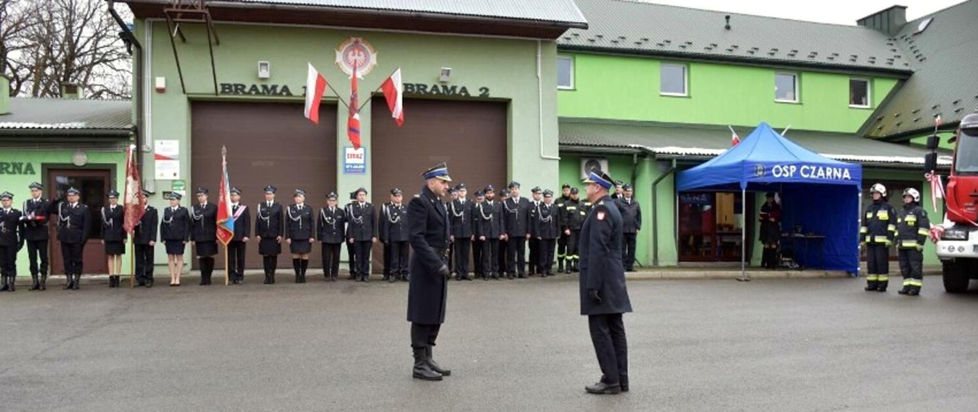 Na zdjęciu widać zastępce jednostki ratowniczo gaśniczej oraz zastępce podkarpackiego komendanta wojewódzkiego PSP na uroczystości przekazania samochodu dla jednostki OSP Czarna. Dowódca składa meldunek komendantowi. W tle druhowie OSP ze sztandarami i w mundurach galowych oraz namiot niebieski z napisem OSP Czarna oraz gminny dom kultury. 