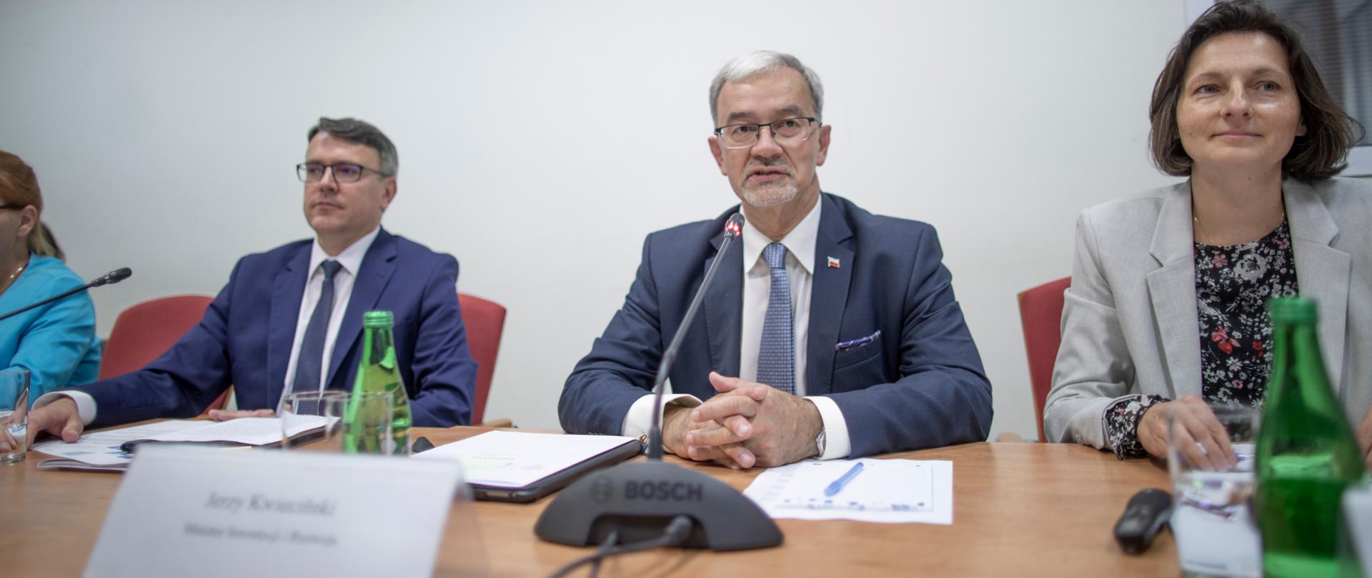 Minister Kwieciński siedzi przy stole przed nim stoi mikrofon, obok siedzą pozostali uczestnicy spotkania