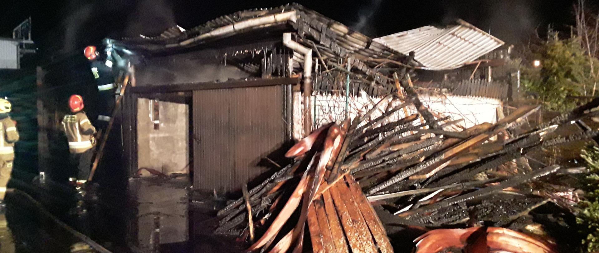 zdjęcie przedstawia pożar budynku gospodarczego w m. Andrespol ul. Teligi . na pierwszym planie widoczne jest składowisko nadpalonych desek , w tle prowadza działania rozbiórkowe strażacy 