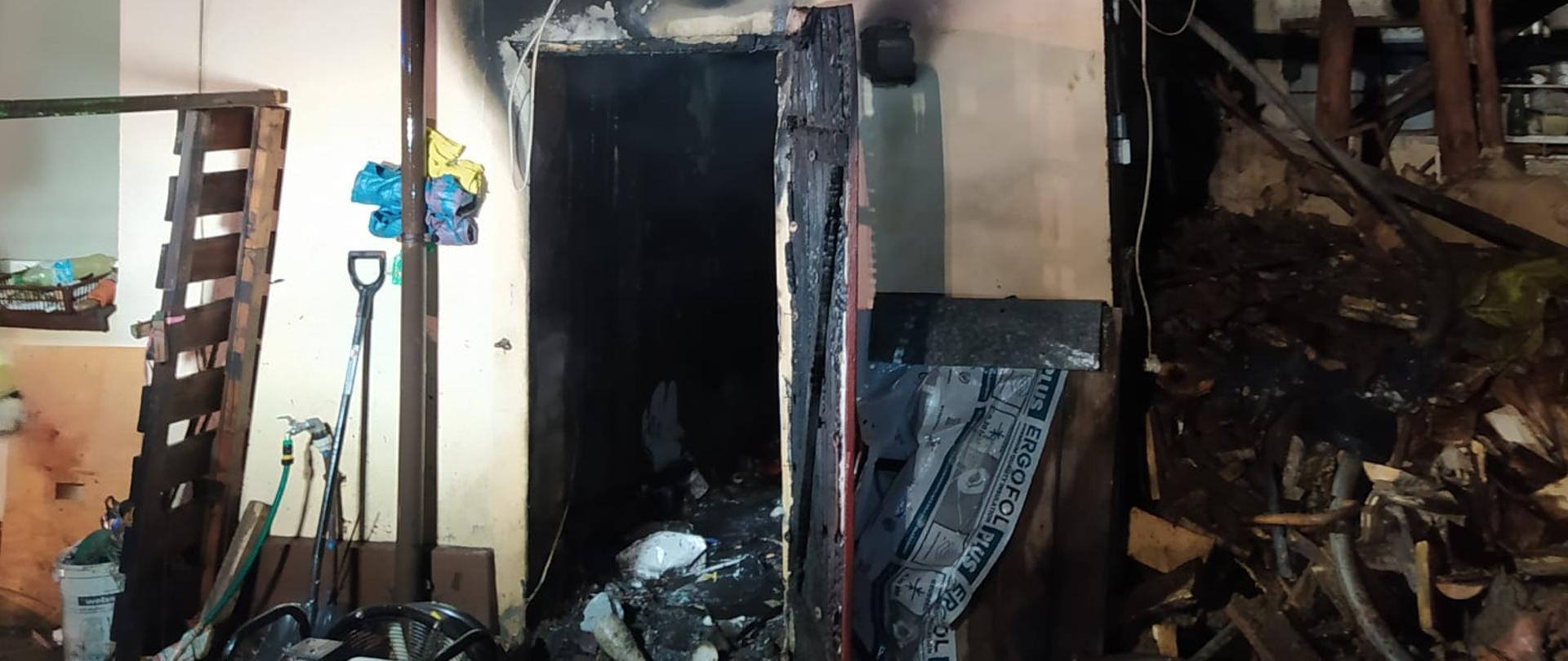 Spalone drzwi do pomieszczenia. Na ziemi śmieci po pożarowe.