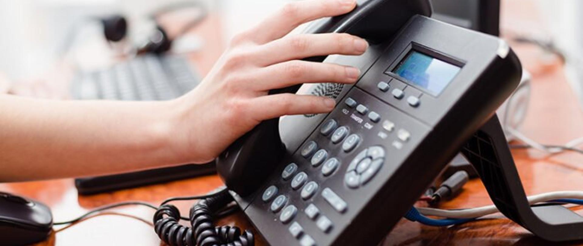 Dłoń dotykająca słuchawki telefonu stacjonarnego