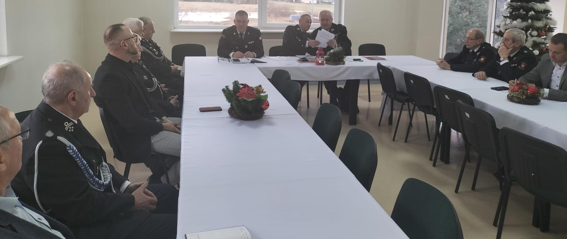 Po prawej i lewej stronie oraz na środku siedzą przy stołach uczestnicy zarządu. W tle okno, a na ścianie nad oknem logo PSP, a na prawo obok godło polski .