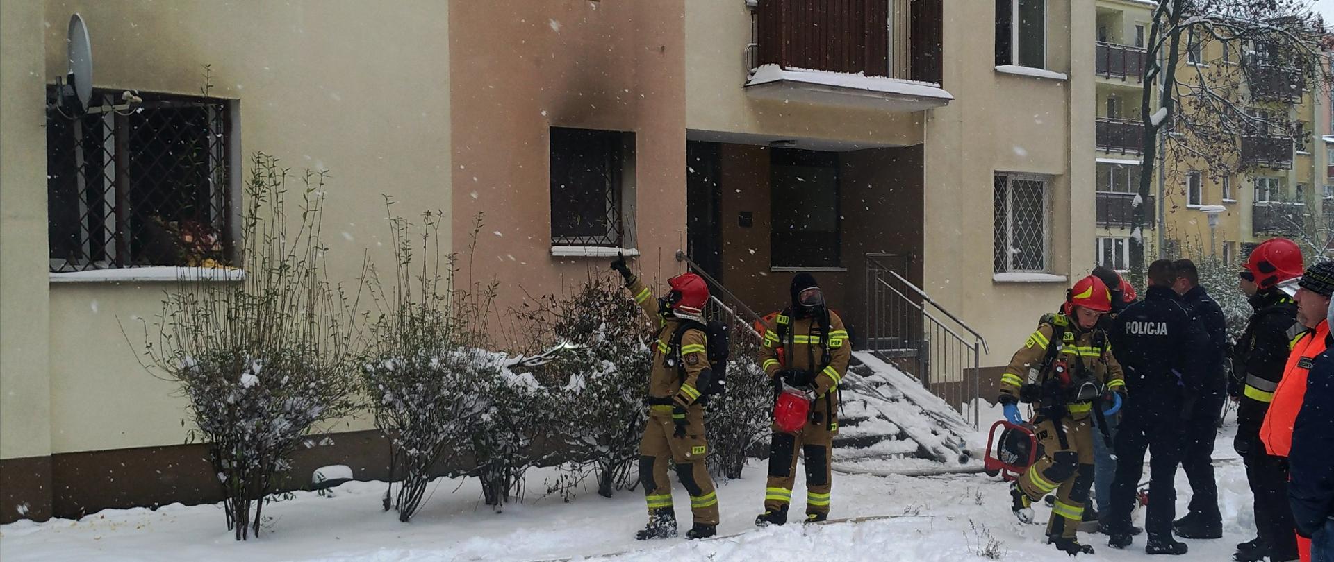 Strażacy wychodzą z budynku po sprawdzeniu klatki schodowej.