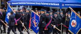 Na zdjęciu widoczny pododdział składający się ze strażaków z Komendy Powiatowej Państwowej Straży Pożarnej podczas defilady z okazji Dnia Strażaka 2023r. Zaproszeni na uroczystość goście w tym mundurowi obserwują defiladę. 