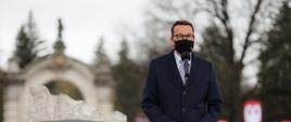 Premier Mateusz Morawiecki stoi przy mikrofonie w tle pomnik.