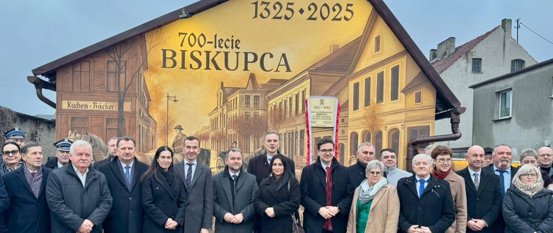 Grupa ludzi stoi przed muralem 