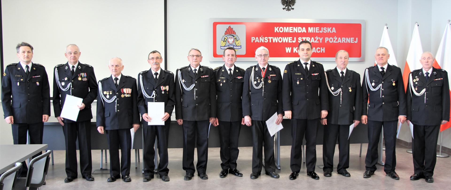 Na zdjęciu przedstawiono grupę 8 strażaków ochotników, którzy otrzymali decyzje o przyznaniu świadczenia ratowniczego. Wśród nestorów pożarnictwa: 8 od lewej świętokrzyski komendant wojewódzki Państwowej Straży Pożarnej w Kielcach st. bryg. Krzysztof Ciosek, 6 od lewej komendant miejski PSP st. bryg. Sławomirem Karwatem i 1 od lewej zastępca komendanta miejskiego PSP bryg. Mariusz Góra.