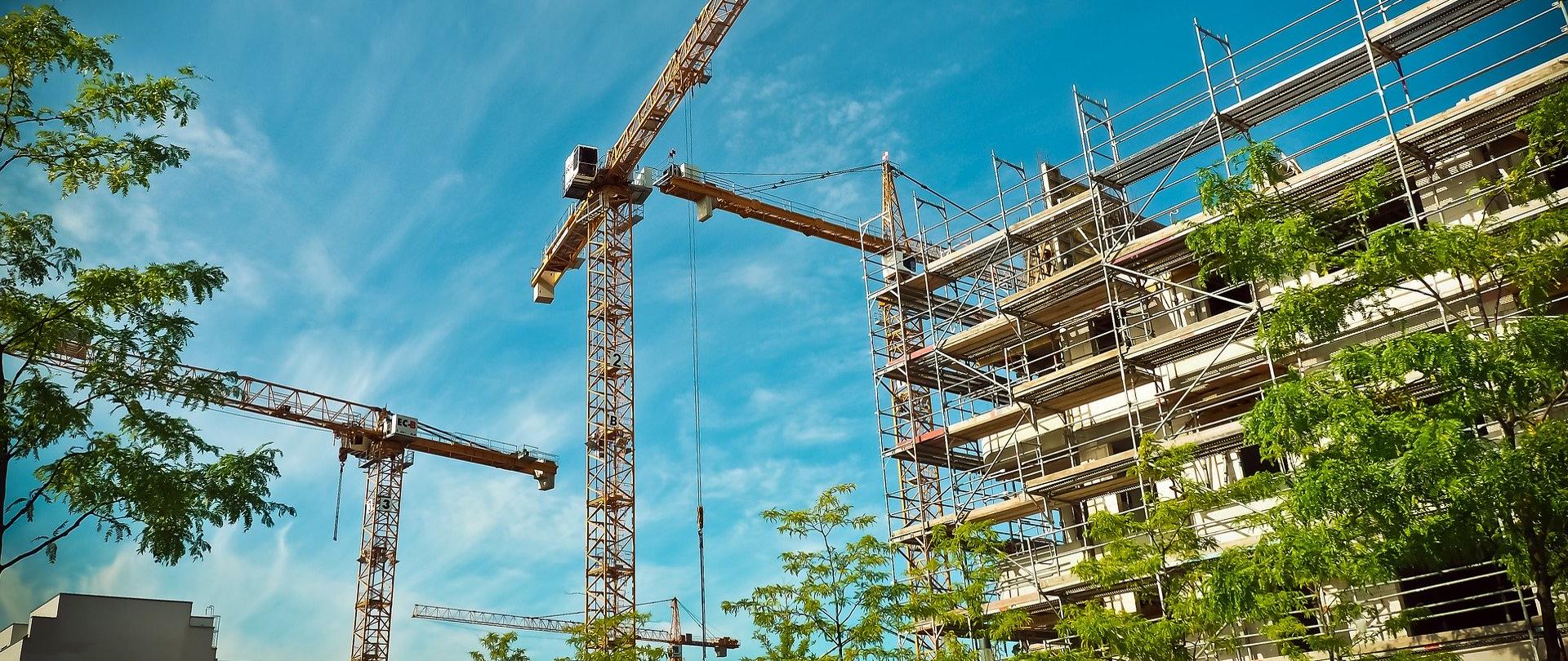 Na zdjęciu plac budowy, żurawie, drzewa.