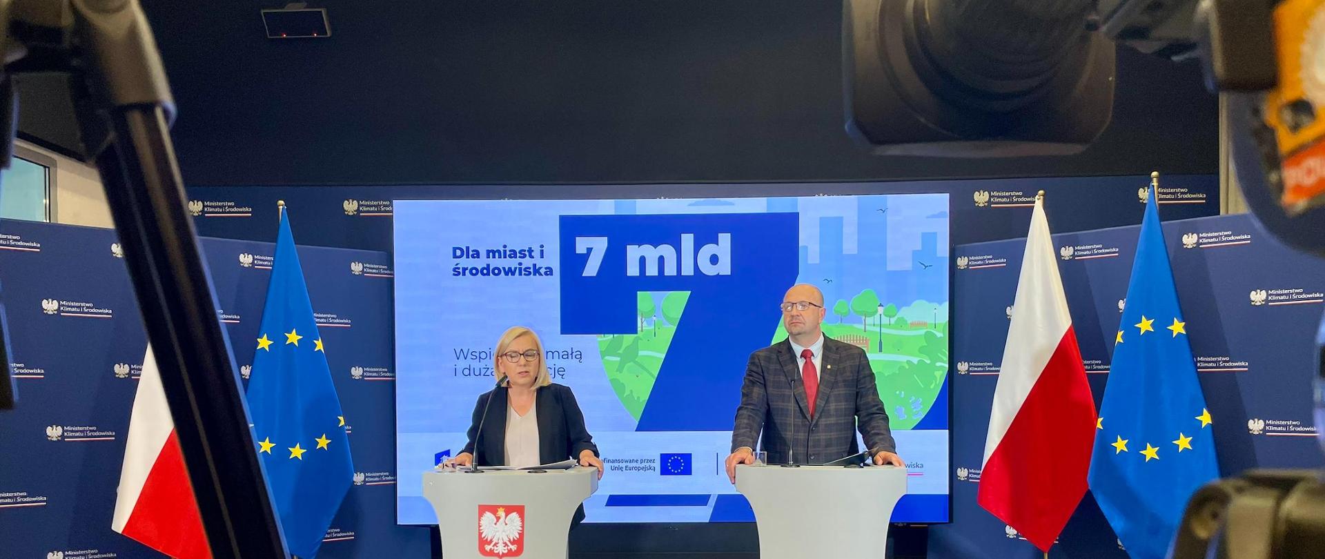 Zdjęcie z konferencji w mkiś, przedstawia panią minister klimatu i wiceprezesa nfośigw Roberta Gajdę na sali konferencyjnej. w głębi sali flagi Polski i UE. Osoby stoją przy pulpitach