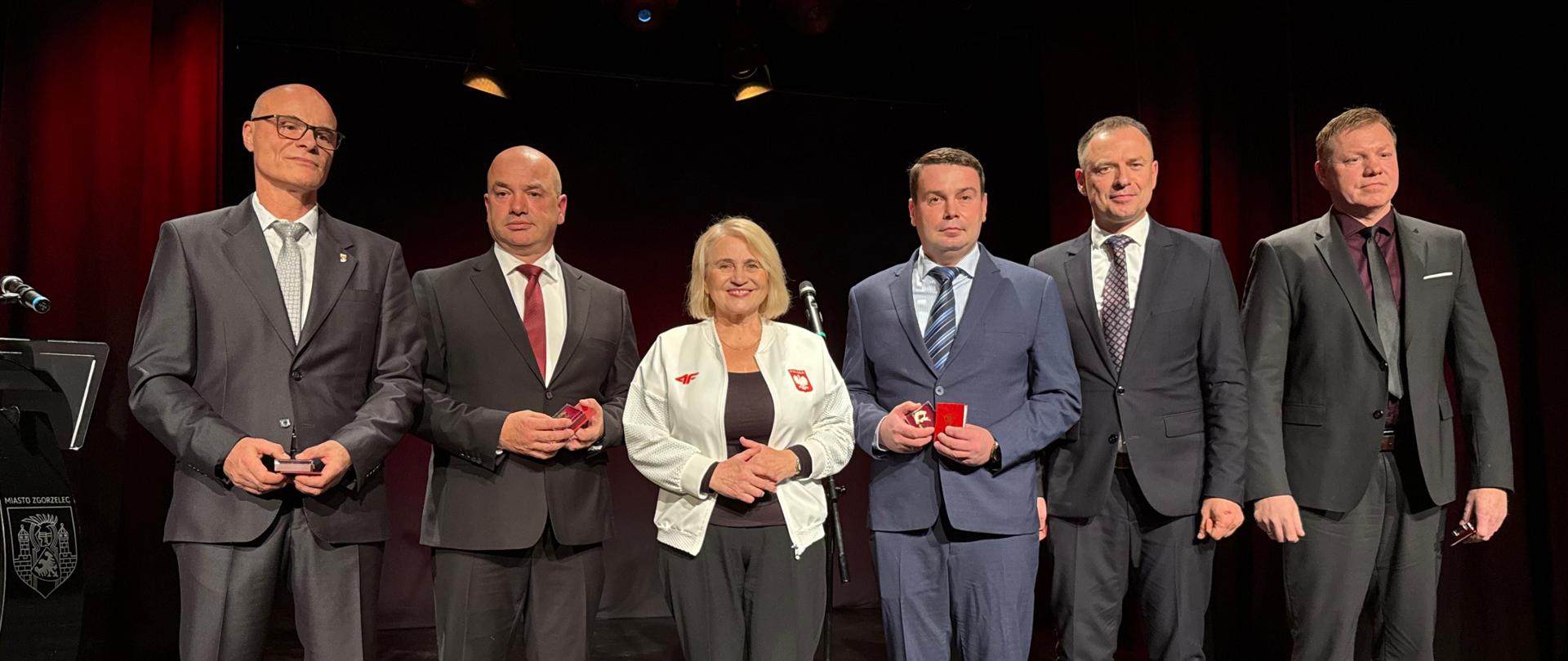 Piotr Borys na jubileuszu klubu MKS Osa Zgorzelec. Zdjęcie grupowe z władzami klubu, stoją na scenie na czarnym tle