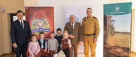 Organizatorzy spotkania stoją wraz z laureatami I grupy wiekowej na tle banerów Komendy Powiatowy PSP w Oleśnie, Starostwa Powiatowego i Nadleśnictwa Olesno w sali konferencyjnej Komendy Powiatowej Państwowej Straży Pożarnej w Oleśnie.