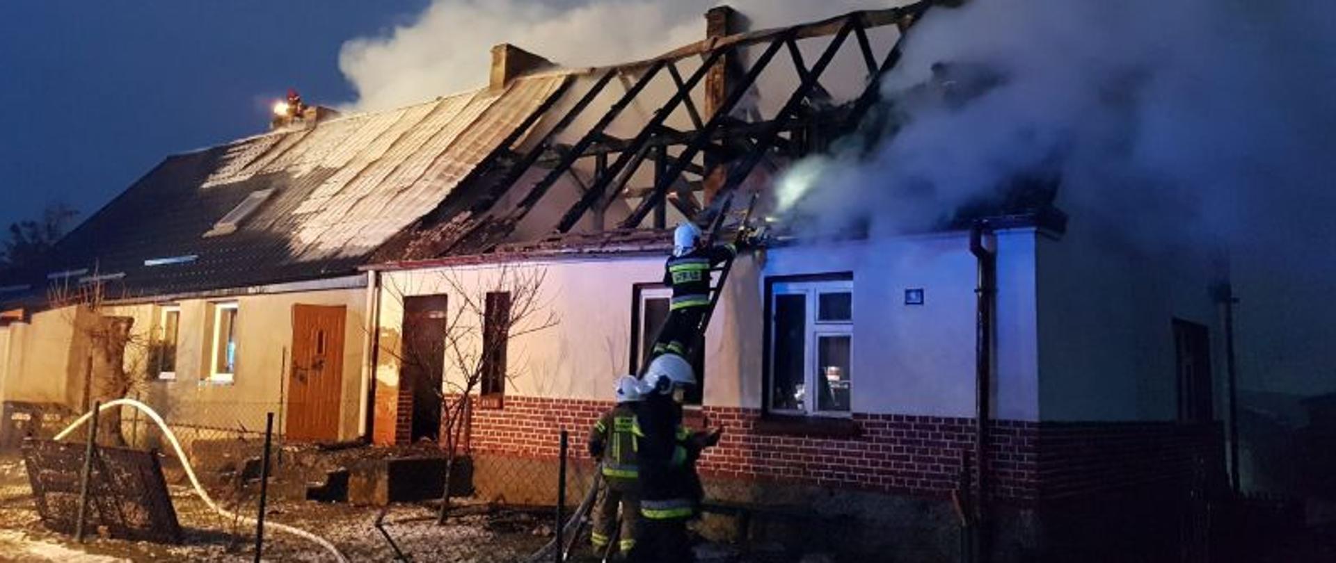 Zdjęcie wykonane w dzień. Widać na nim budynek po ugaszeniu pożaru. Budynek wielorodzinny z dwuspadowym dachem. Połowa dachu jest całkowicie spalona. Brak pokrycia dachowego , widać okopcone krokwie o deski
