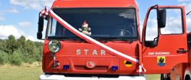 Zdjęcie przedstawia samochód ratowniczo-gaśniczy marki STAR koloru czerwonego, z przewieszoną biało-czerwoną wstęgą oraz otwartymi drzwiami od strony kierowcy, na których widnieje napis OSP Żukówko oraz herb Gminy Parchowo
